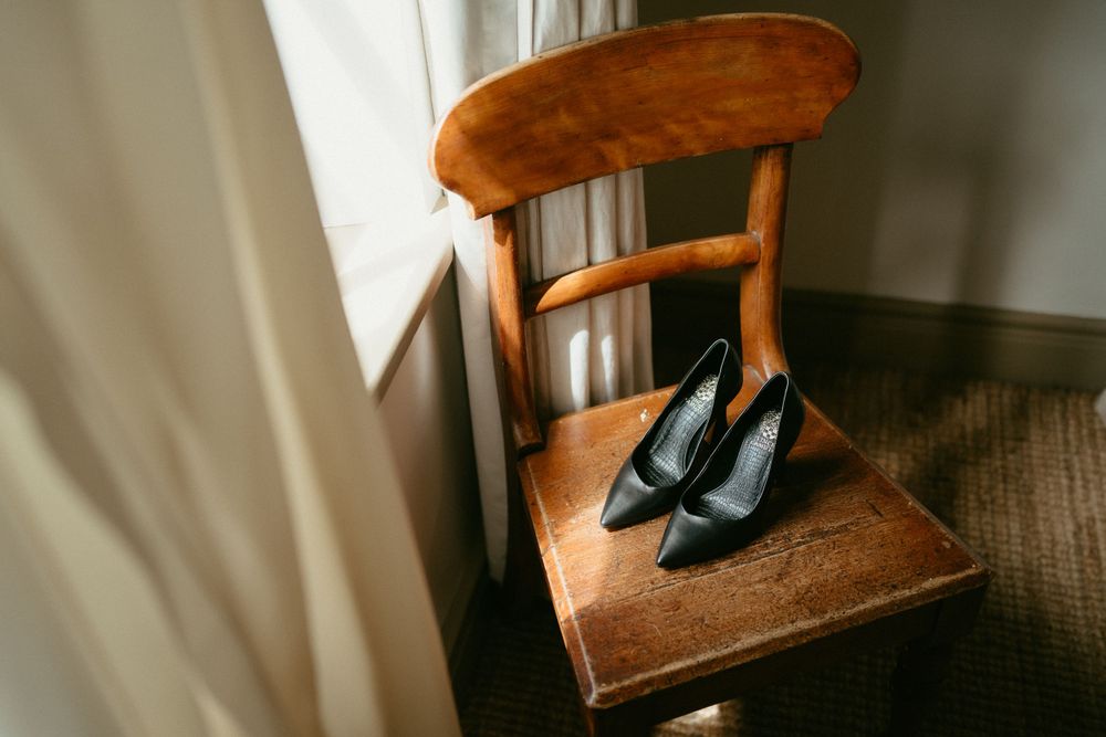 Navy blue heels placed on wooden chair by window light.