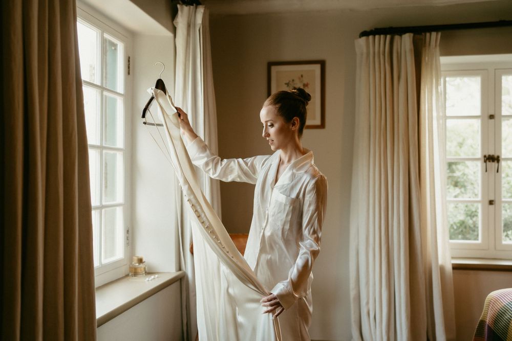 Morning light streams through windows as preparations begin with a white dress near curtains.