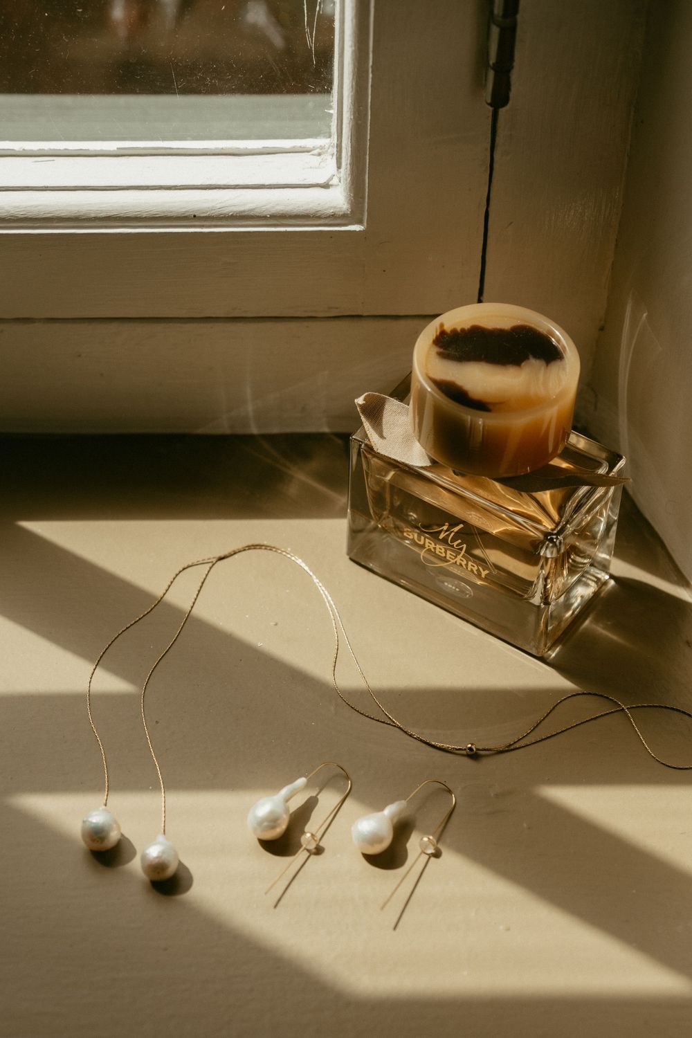 Elegant perfume bottle and earbuds casting shadows near a window in warm sunlight.