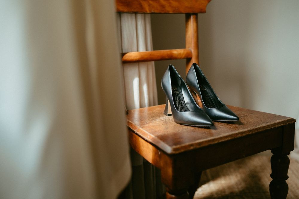 Pair of black high heel shoes placed on wooden chair in natural lighting.