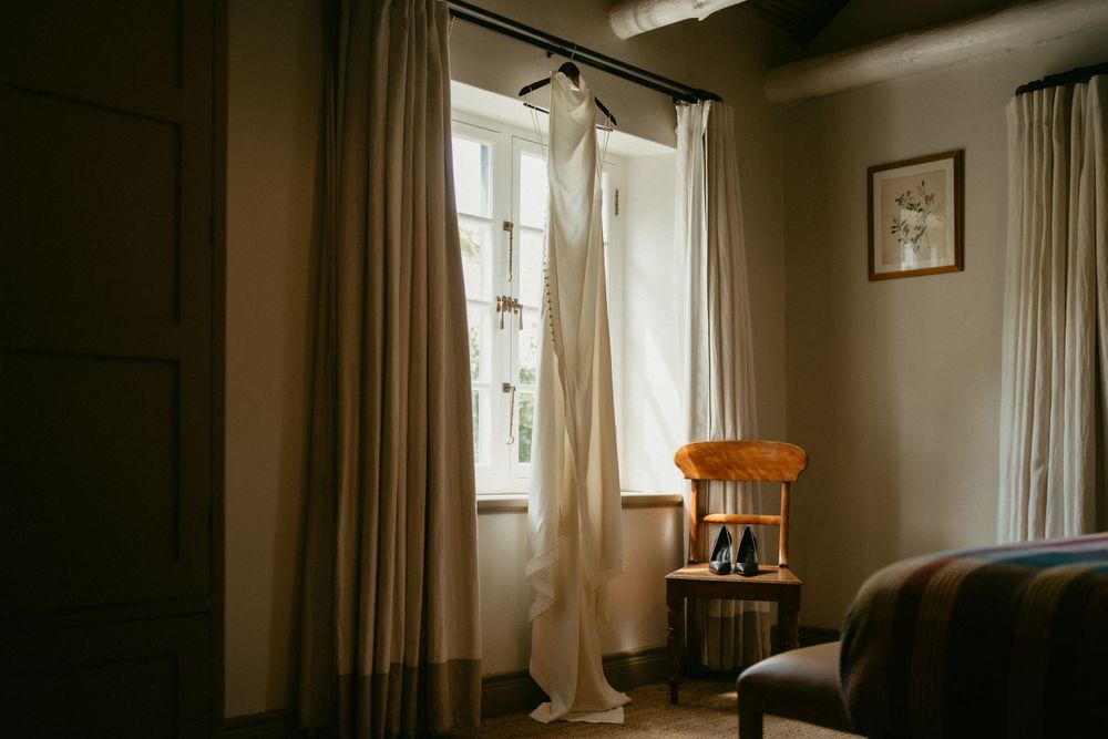 Wedding dress hanging by window in natural light with chair in corner.