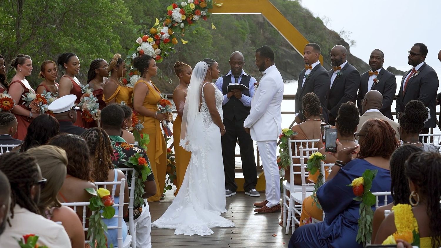 A young couple stands in front of water looking at each other while holding hands in example of wedding videography.