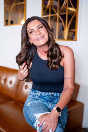 Woman in navy tank top and distressed jeans sitting on brown leather couch.