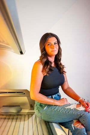 Woman in black tank top sits on tanning bed in casual pose.