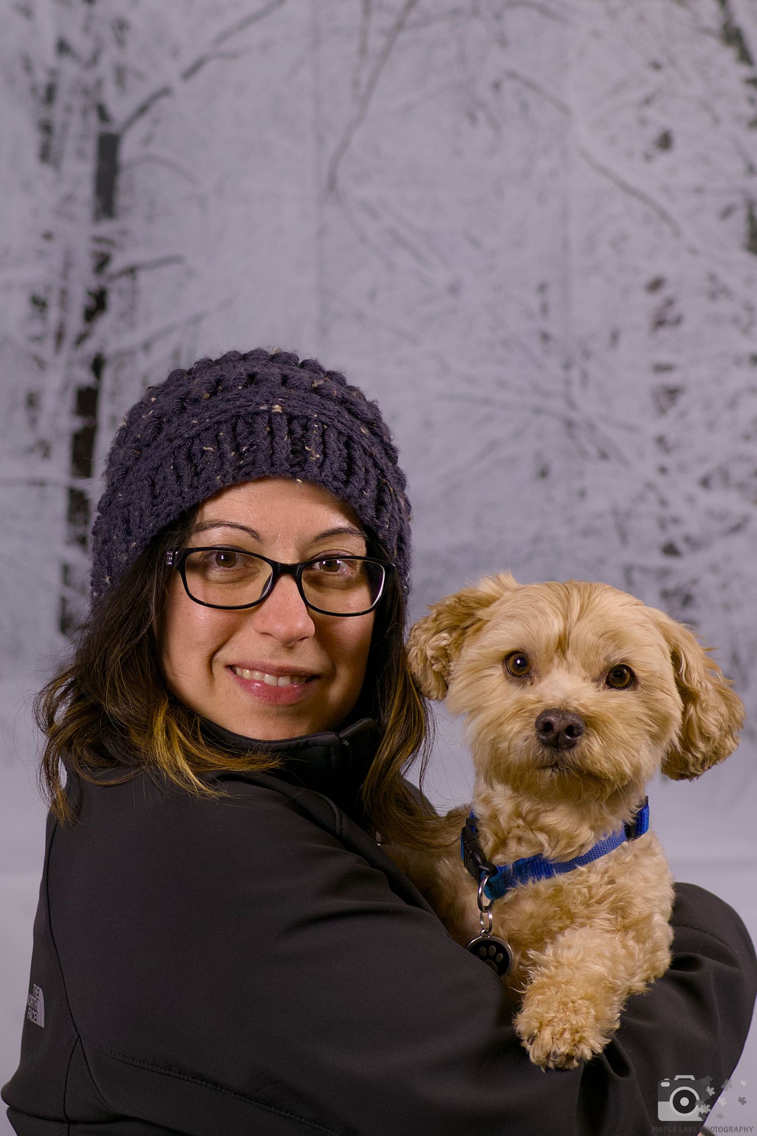 An adorable goldendoodle puppy with tan fur wearing a blue collar is held outdoors in a winter setting.