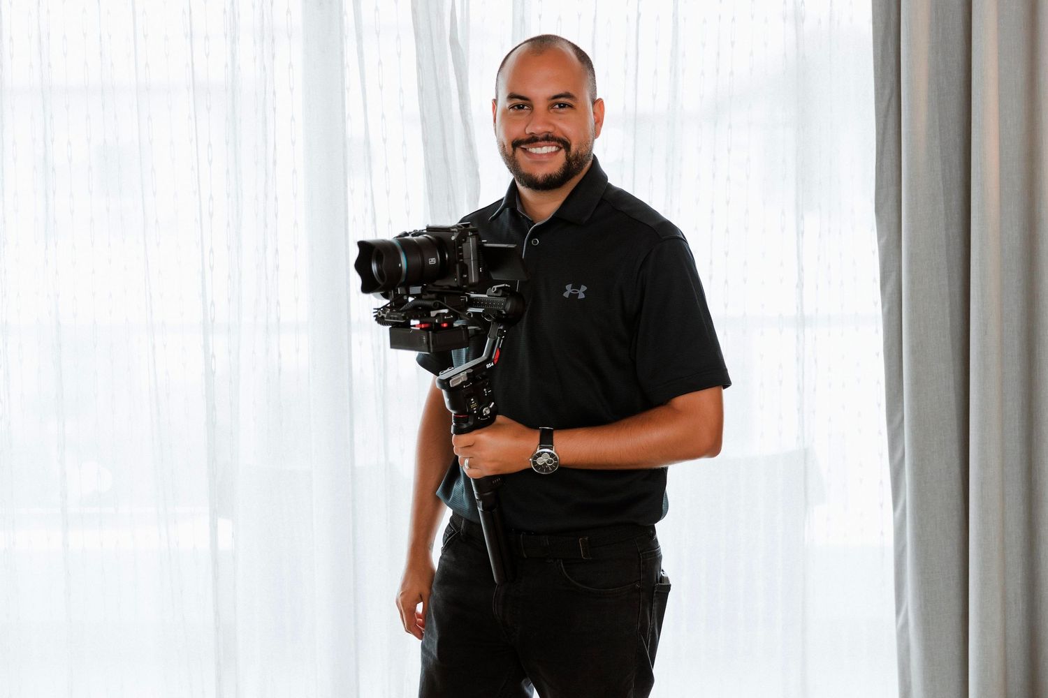 Professional videographer in black attire holding cinema camera against bright background.
