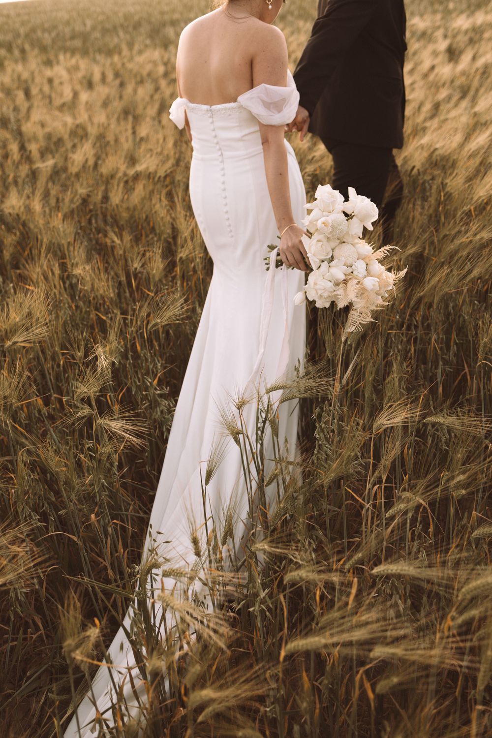 Elegant white wedding dress and floral bouquet silhouetted against a golden wheat field.