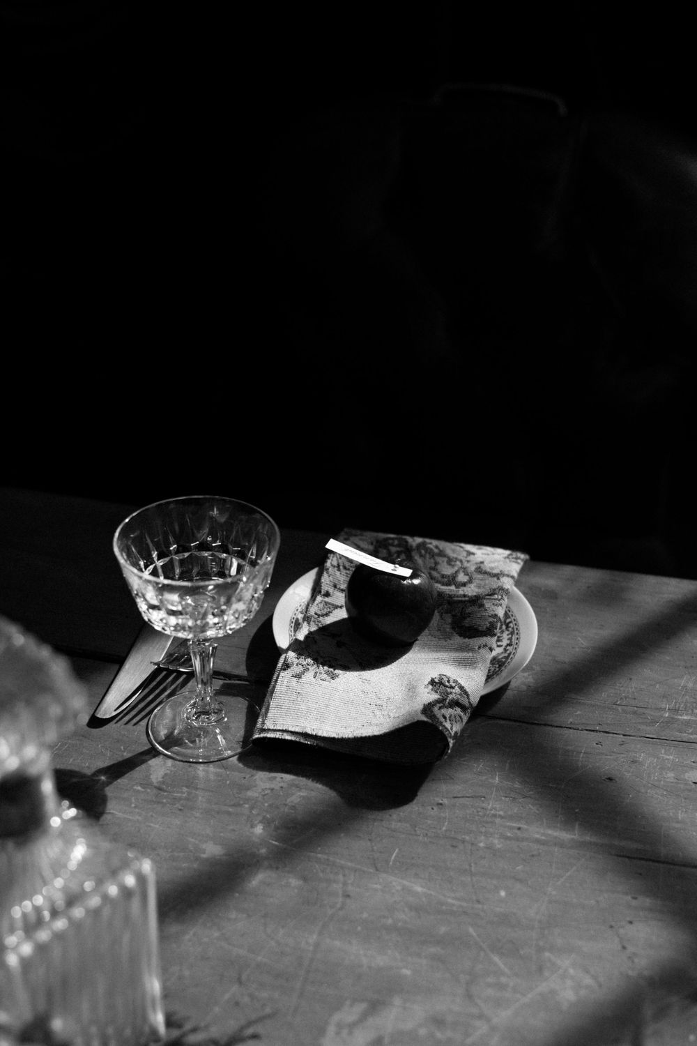 Moody black and white photo of crystal glassware on wooden surface.