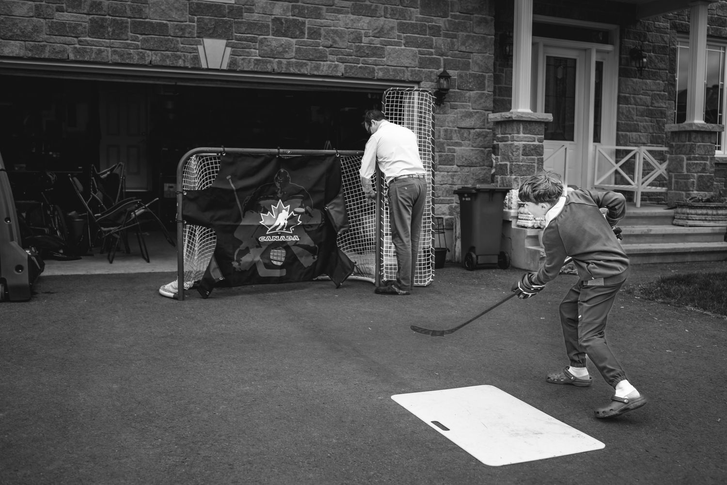A young man shoots a puck toward the net in his driveway as his father completes attaching a section.