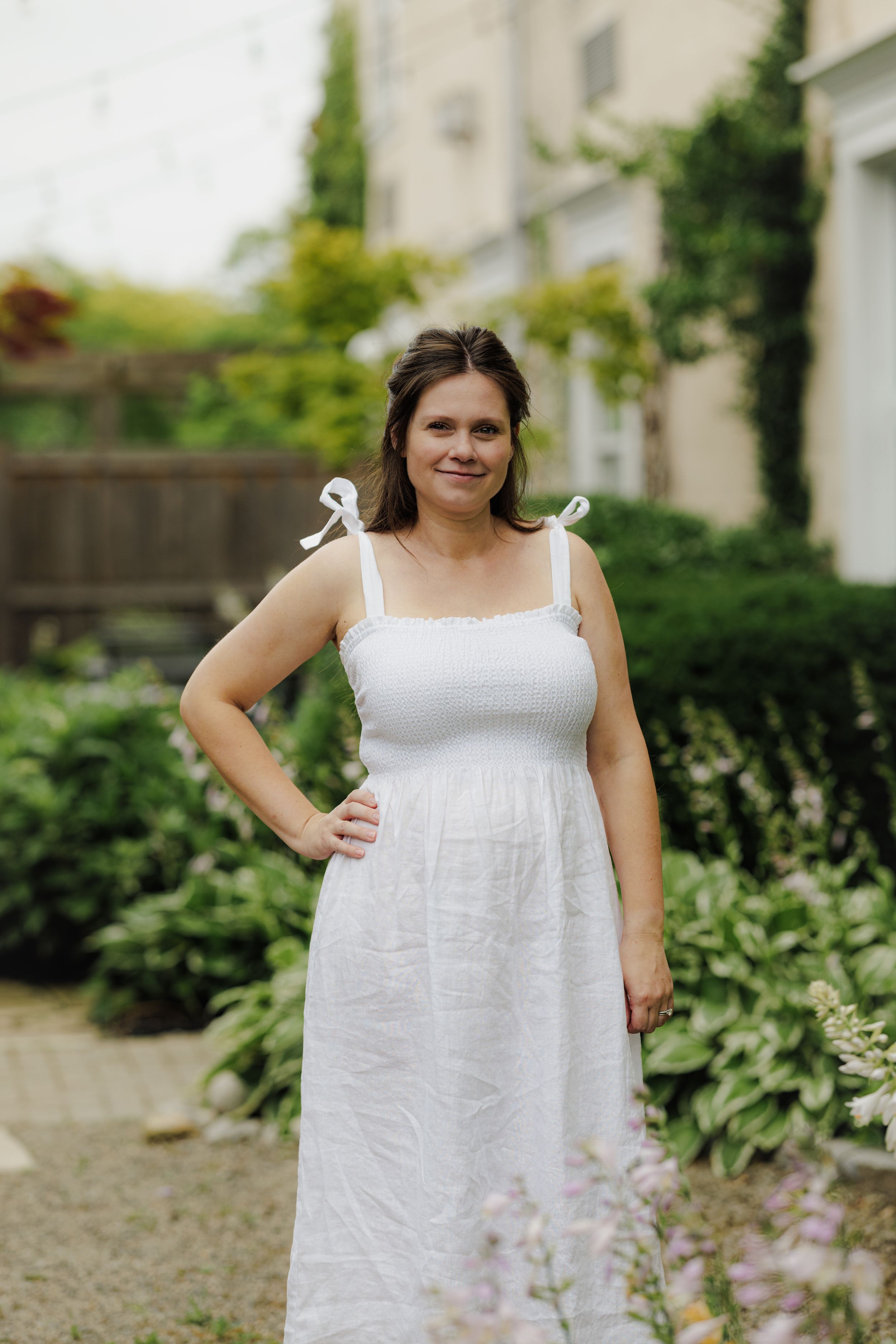 A white cotton sundress with bow tie straps photographed in a lush garden setting.
