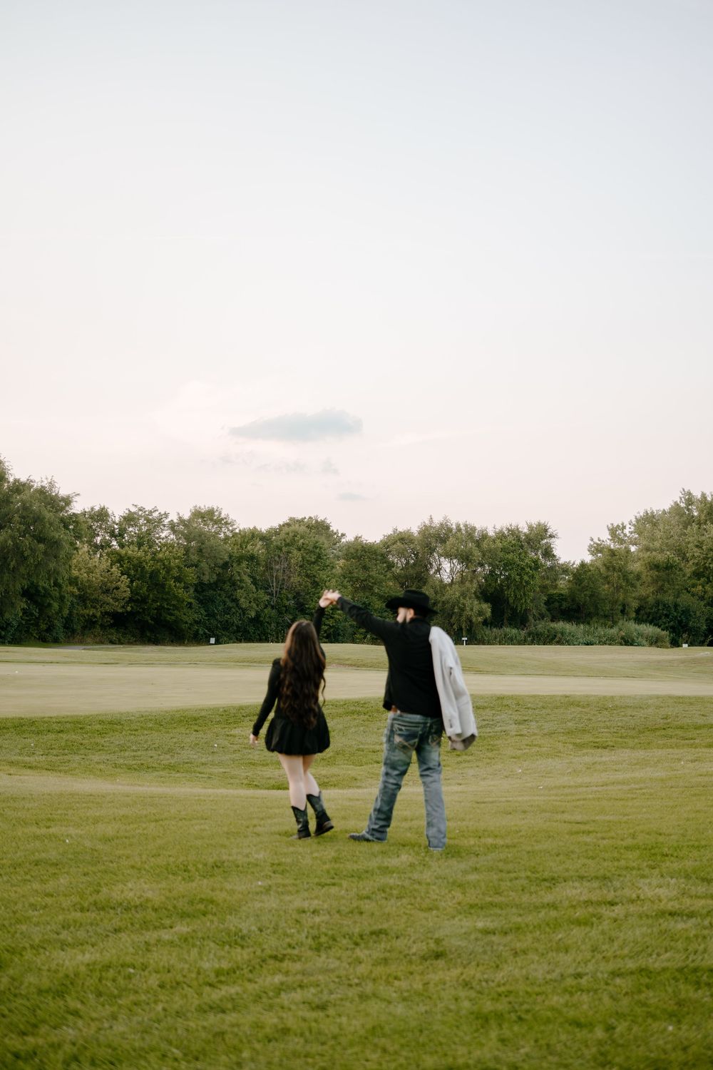 Two people walk together across a grassy field on an overcast day.