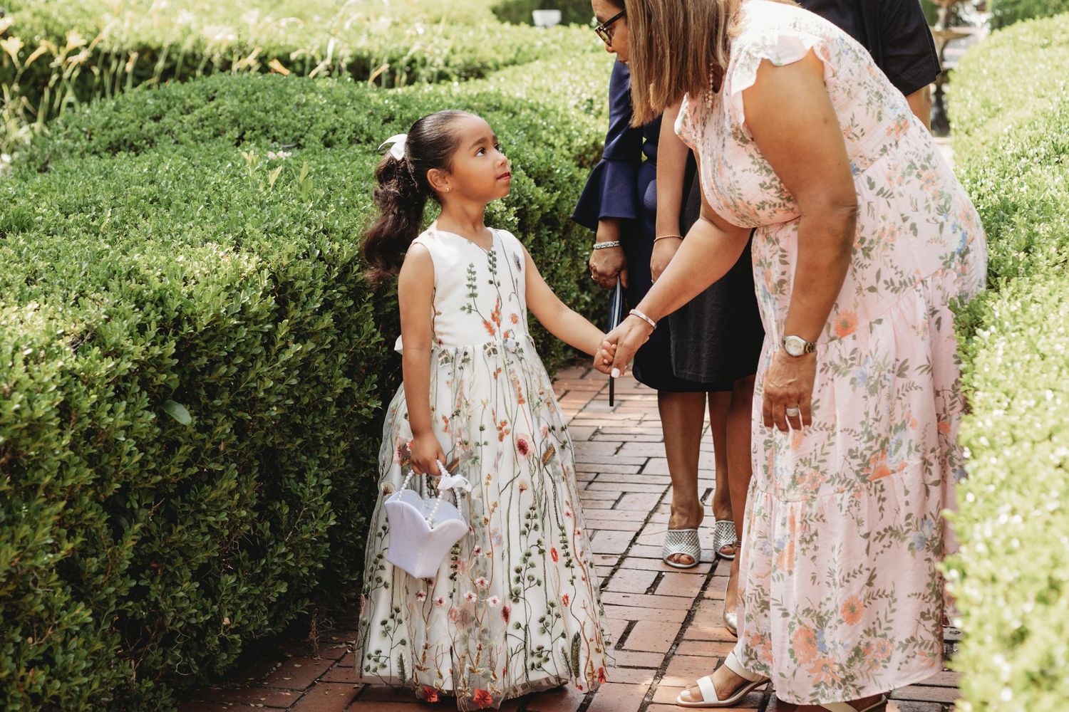Wedding party in floral dresses walking along an outdoor garden path.