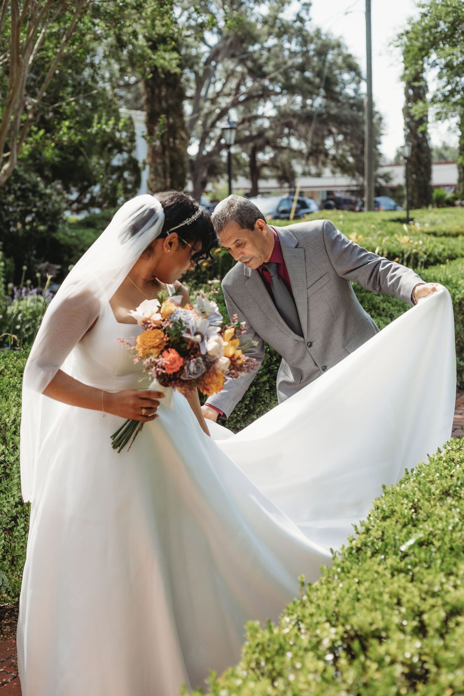 Elegant wedding dress flowing in the breeze against a green garden backdrop.