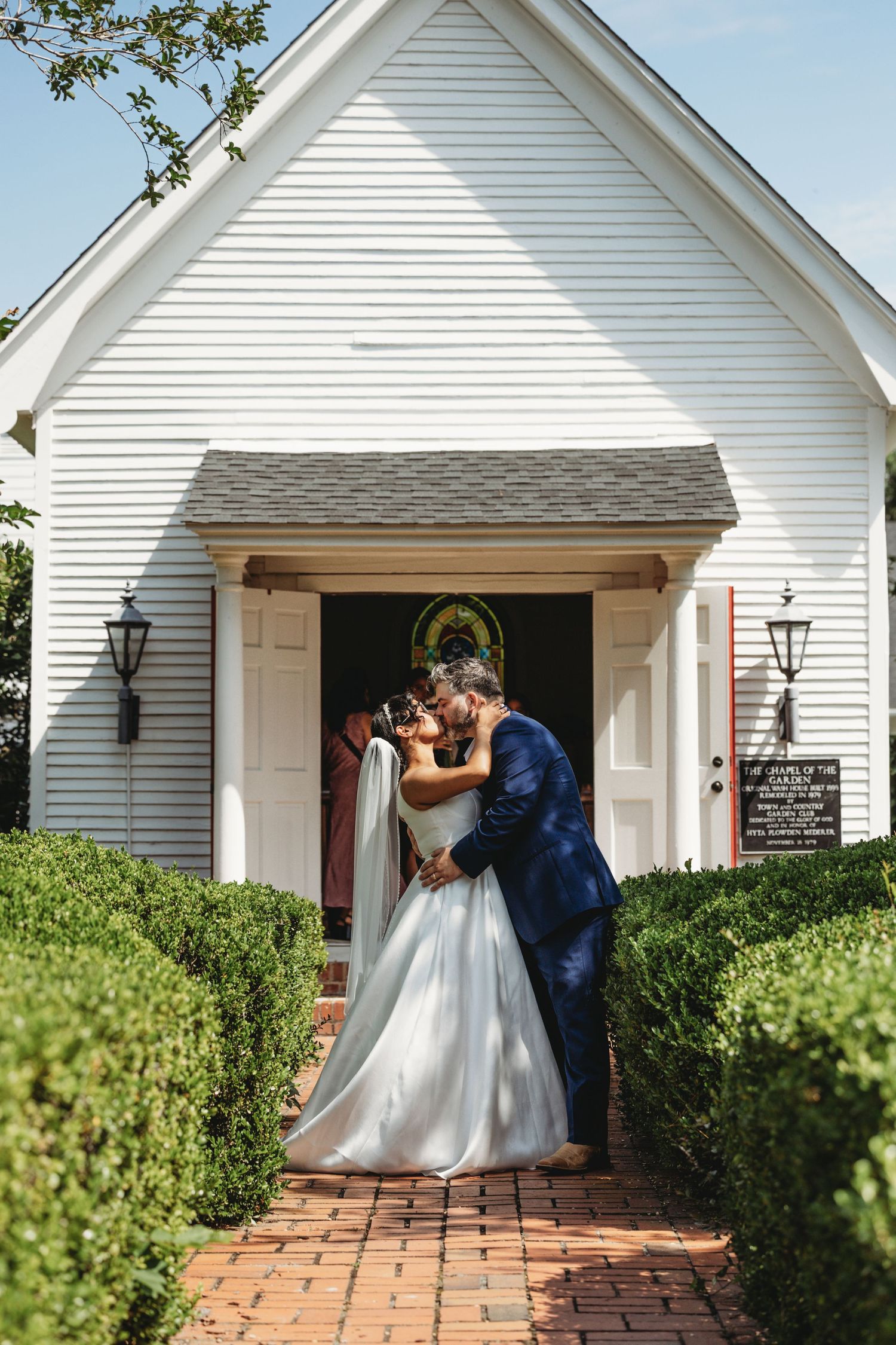A romantic moment captured outside a charming white chapel with brick walkway.
