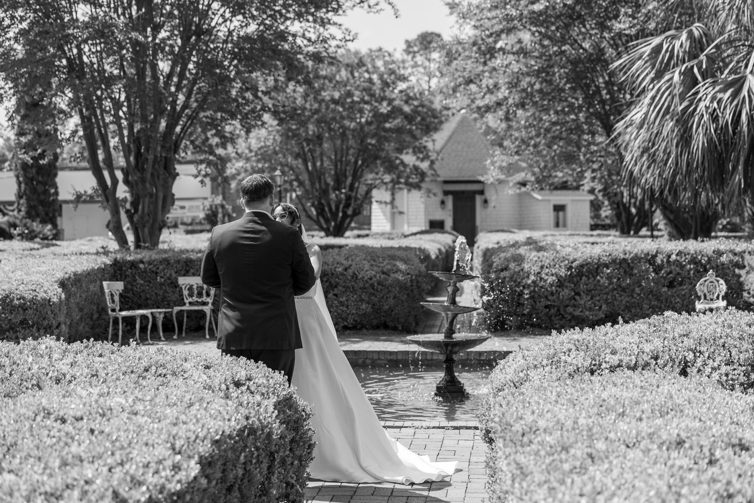 Wedding couple walking through a scenic garden path lined with trees and greenery.