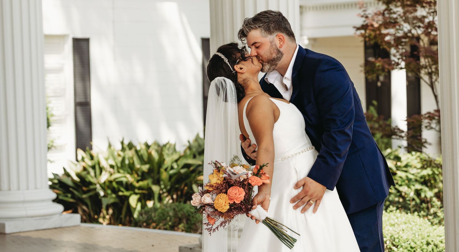 Wedding couple poses together on an elegant white columned porch.