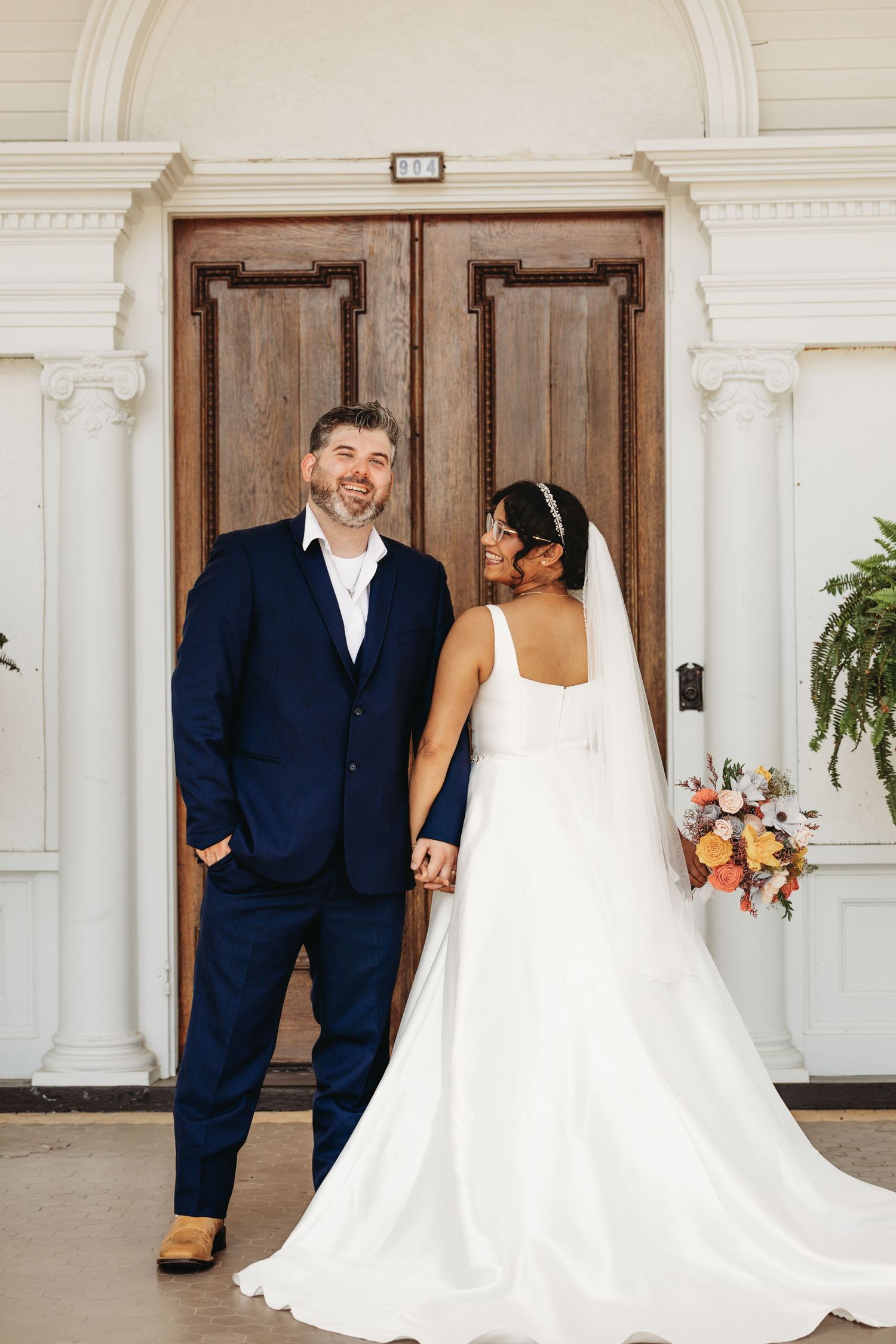 Wedding couple shares playful moments in front of a white colonial-style building entrance.