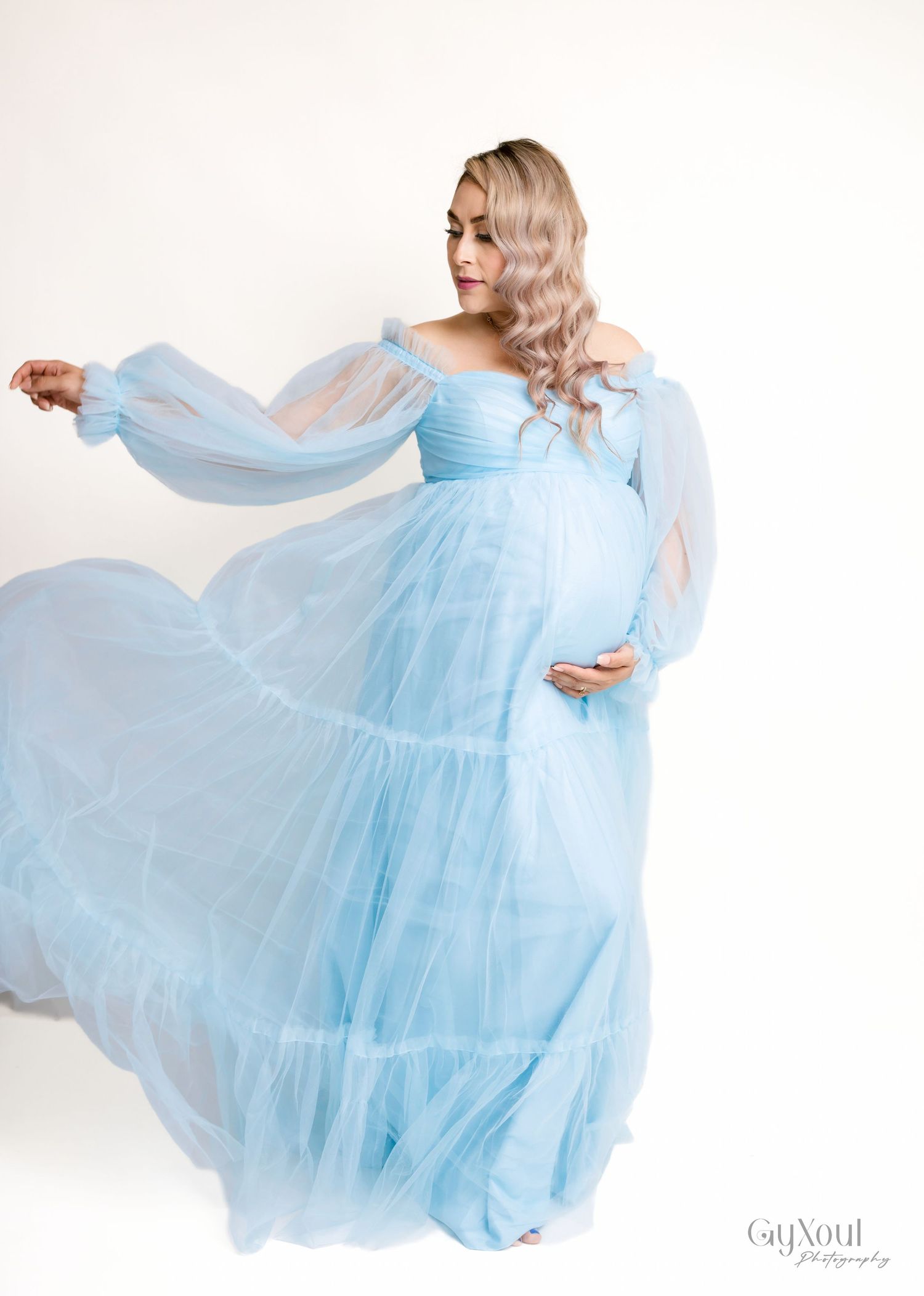 Ethereal powder blue tulle maternity gown with long sheer sleeves flows gracefully in a studio setting.