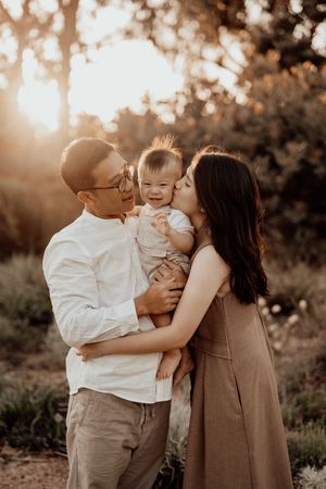 A family shares a tender moment together outdoors during golden hour sunset with soft bokeh lighting in the background.
