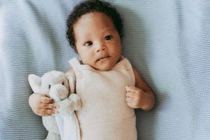 Baby lying on light blue textured fabric wearing white onesie, gazing upward with peaceful expression.