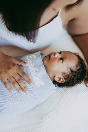 A tender parenting moment shows a baby in a blue onesie being cradled on white textured fabric.