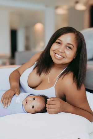 A mother and small baby lying together on a white bed, sharing a sweet bonding moment in a cozy setting.