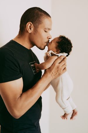 A tender parent-baby bonding moment captured in a minimalist studio setting with white backdrop.