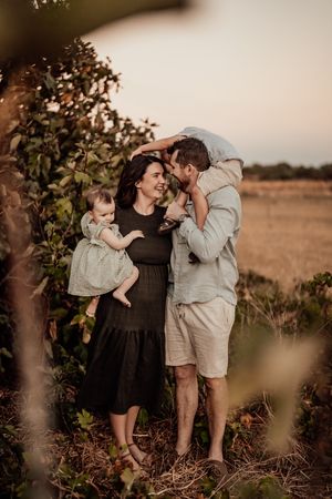 Warm sunset photo of a loving family embrace outdoors in a field with shrubs and soft golden lighting.