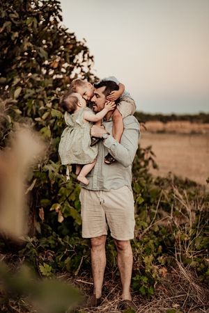 Two young siblings share sweet moments together outdoors at sunset in matching beige outfits against a natural backdrop.