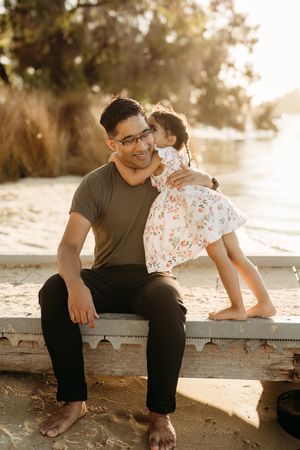 A tender moment captured between two people sitting on a concrete ledge at sunset with warm golden lighting.