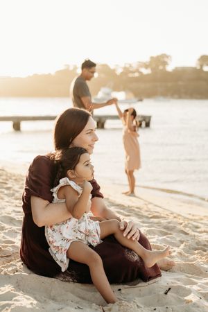 Family enjoying a peaceful sunset moment together on a sandy beach with golden light streaming across the water.