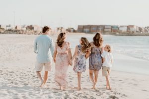 A group walks together on the beach at sunset wearing light colored clothing and holding hands.