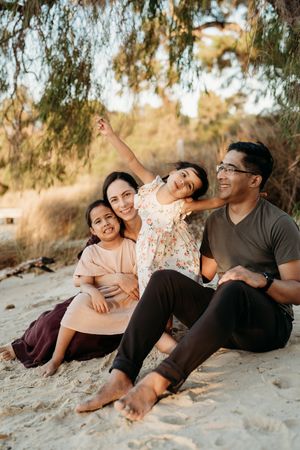 Family sitting together on sandy beach during golden hour enjoying playful moments in nature.