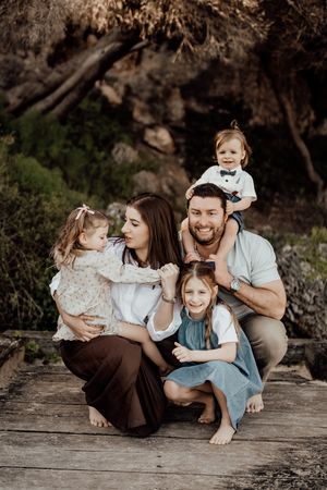 Family posing together for a warm outdoor portrait on wooden deck in natural setting.