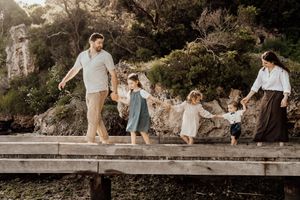 Family holding hands while walking together on a wooden dock by the water during golden hour.