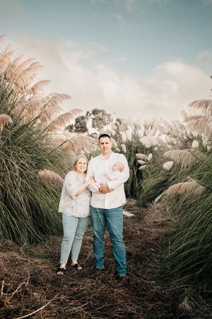 A family stands together on a dirt path surrounded by tall pampas grass and cloudy skies during sunset.