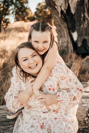 A joyful moment of hugging and laughter wearing matching floral dresses in a warm sunlit outdoor setting.