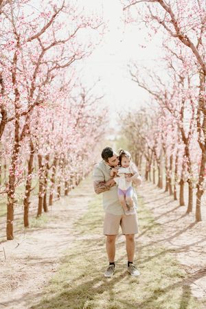 A magical moment captured in a blooming cherry blossom orchard with pink flowers creating a romantic pathway.