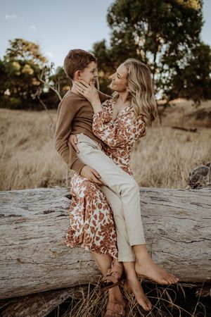 Romantic couple sitting on rustic log during golden hour photoshoot in autumn field setting.