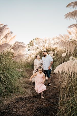 A family walks along a dirt path surrounded by tall pampas grass during golden hour.