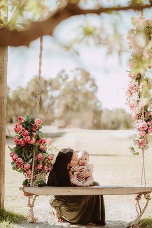 A dreamy garden scene with a floral-decorated wooden swing beneath blossoming trees in soft sunlight.