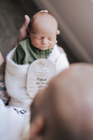 Close-up view of a sleeping newborn baby wrapped in white swaddle against a soft blurred background.