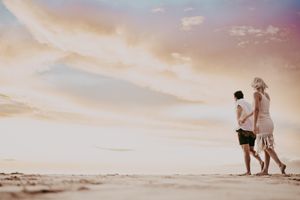 Two people sharing a romantic moment while walking on a sandy beach at sunset.