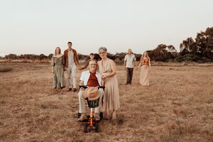 Group in elegant neutral attire poses for wedding photos in an open field at golden hour.