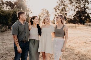 Four friends laughing together outdoors in warm sunlight during golden hour in a natural field setting.