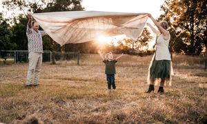 A group of people dance together in a golden field at sunset with dust particles creating a dreamy atmosphere.