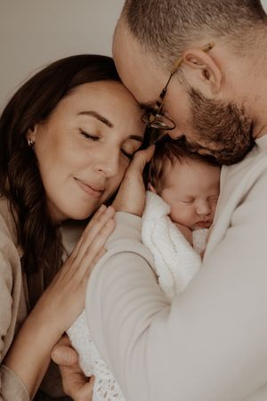 Intimate family portrait showcasing a tender moment between parents and their sleeping newborn baby in soft lighting.