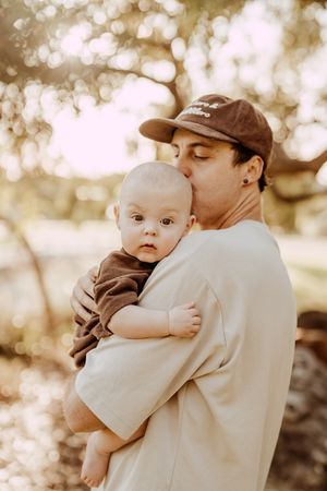 A tender outdoor portrait of parent and infant with soft bokeh background in warm sepia tones.
