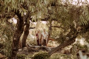 Two people stand under the shade of green trees in a serene woodland setting captured in a vintage-style photograph.
