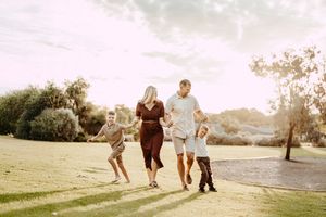A family running together on a grassy hill during golden hour with mountains in the background.
